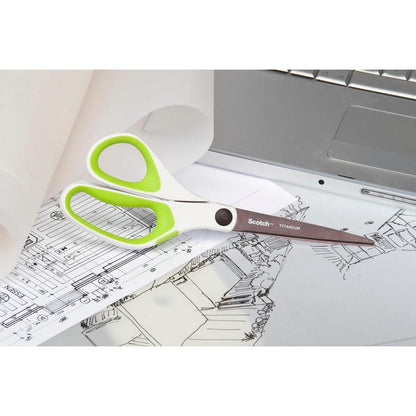 Egy pár Scotch™ titánium olló, 20 cm, a 3M Deutschland GmbH-tól, fehér és zöld fogantyúkkal, építészeti rajzokon pihen egy ezüst laptop és egy tekercs átlátszó papír mellett.