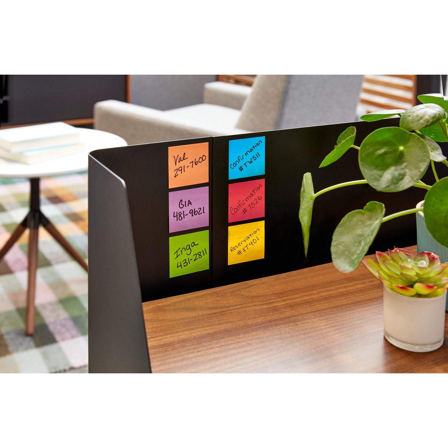 Auf einem hölzernen Schreibtisch stehen fünf bunte Post-it® Super Sticky Z-Notes (76 x 76 mm, 90 Blatt/Block) von 3M Deutschland GmbH. Neben ihnen stehen eine Topfpflanze und eine Sukkulente. Im Hintergrund: Tisch, Stühle, Karoteppich.