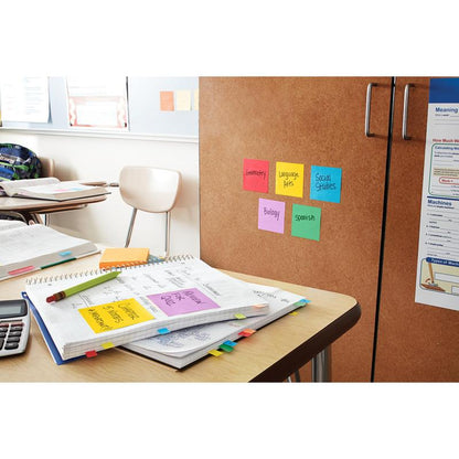 Egy osztálytermi íróasztal jegyzetfüzetekkel, számológéppel és színes jegyzetlapokkal. Egy szekrényen 3M Post-it® jegyzetlapok (sárga, 76x76mm, 90 lap/blokk, 6 blokk/csomag, 100% PEFC) vannak felcímkézve: Geometria, Nyelvtudomány, Társadalomtudomány, Biológia és Spanyol.